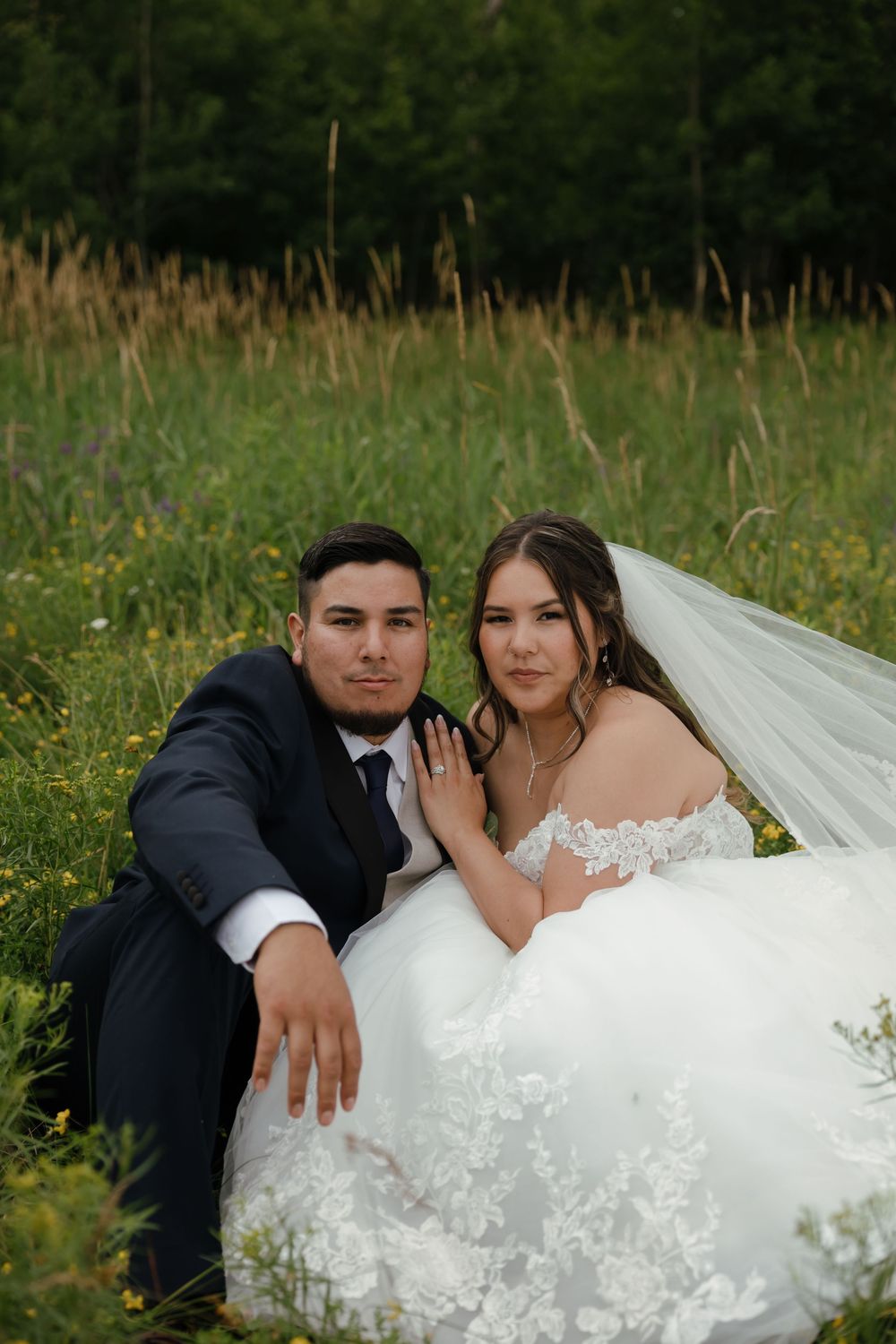 A couple dressed in wedding attire poses together in a field of yellow wildflowers.
