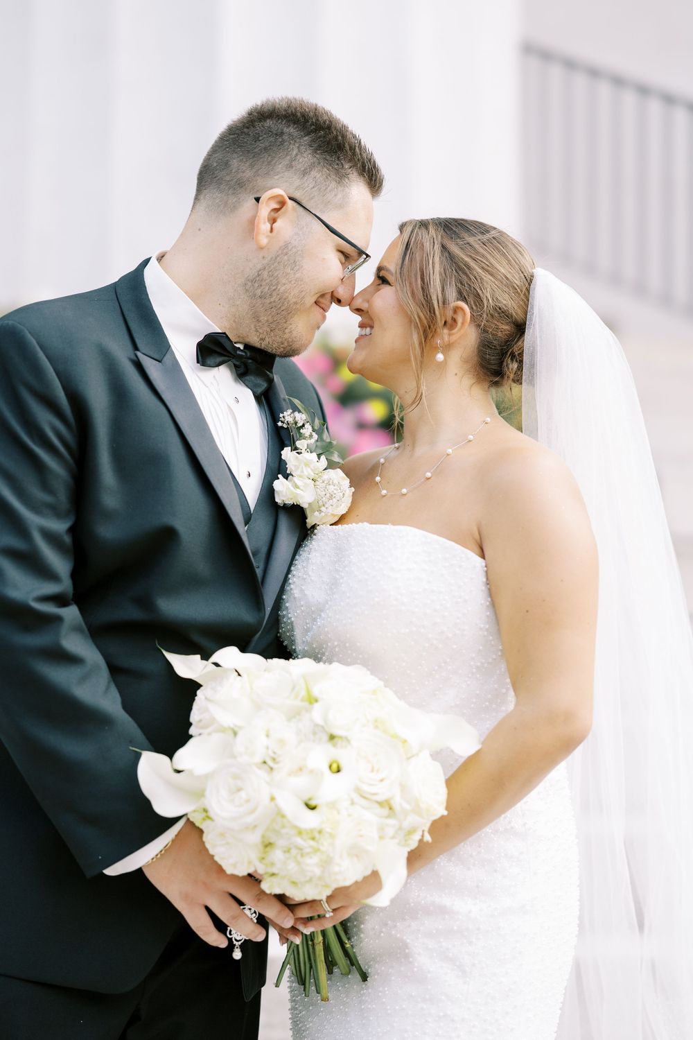 A romantic wedding moment with a white bouquet of roses, featuring a groom in a black tuxedo and bride in a white gown.