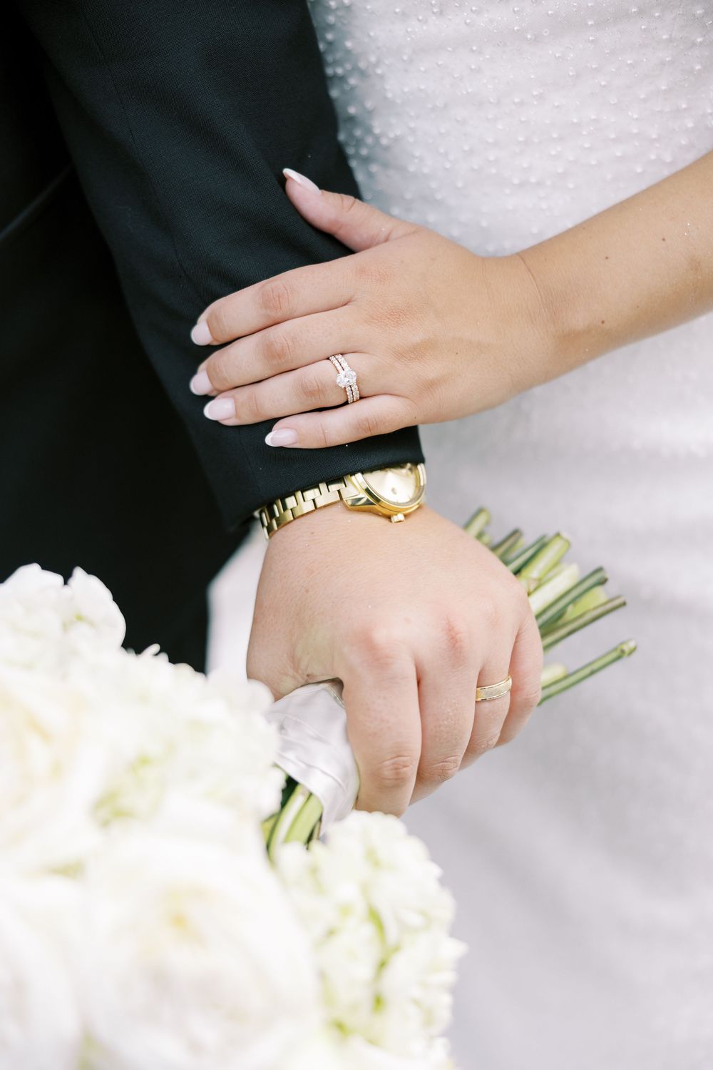 Wedding ring details shown in sequence as hands hold white floral bouquet against black and white formal attire.