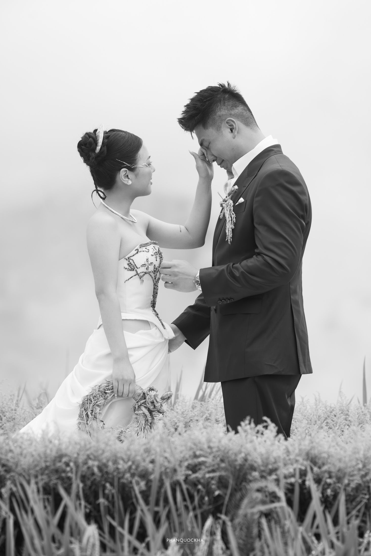 Black and white photo of bride tenderly touching grooms face in romantic rice field setting.