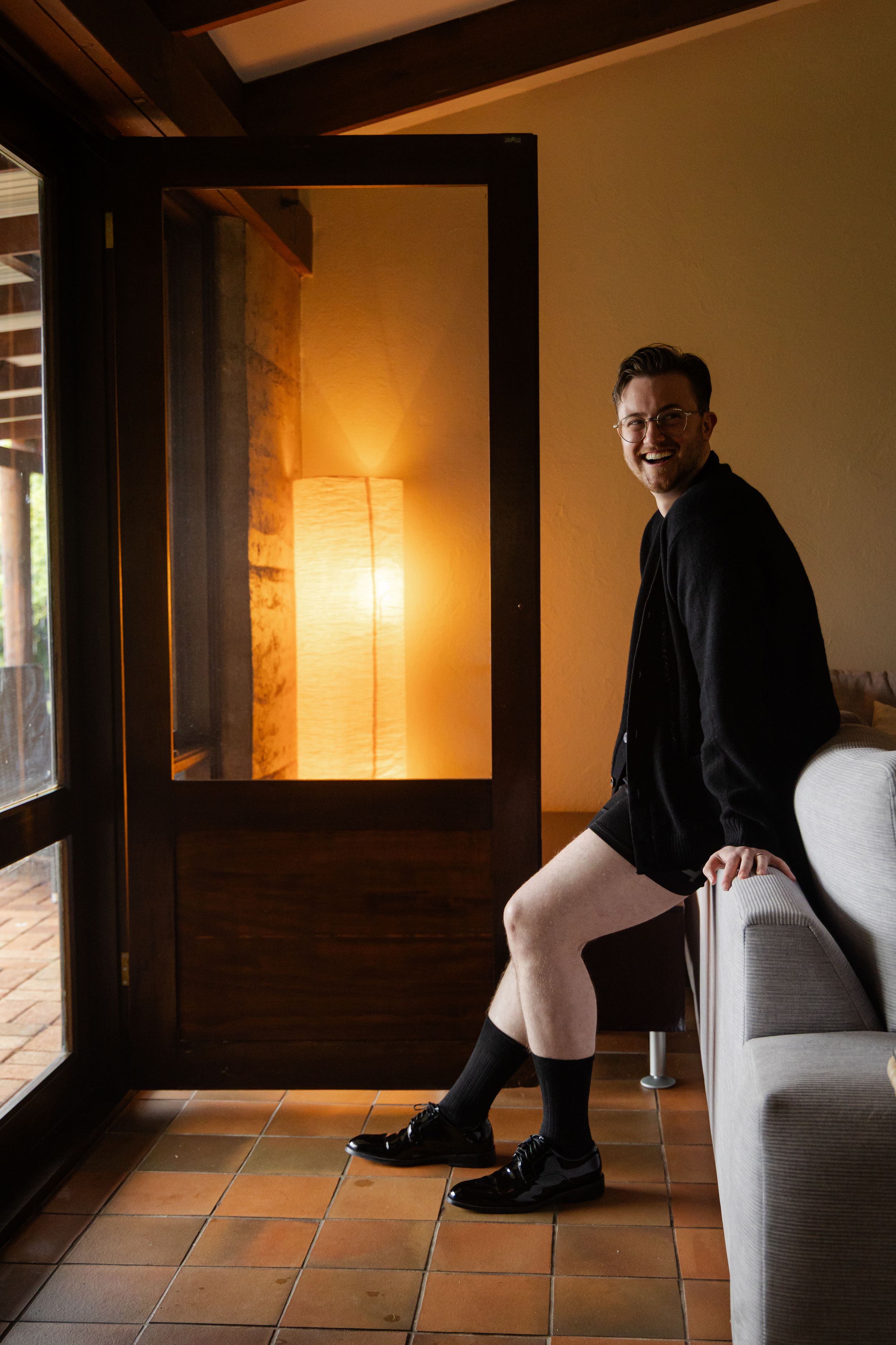 Candid photography of groom getting ready for his wedding, leaning on a couch laughing