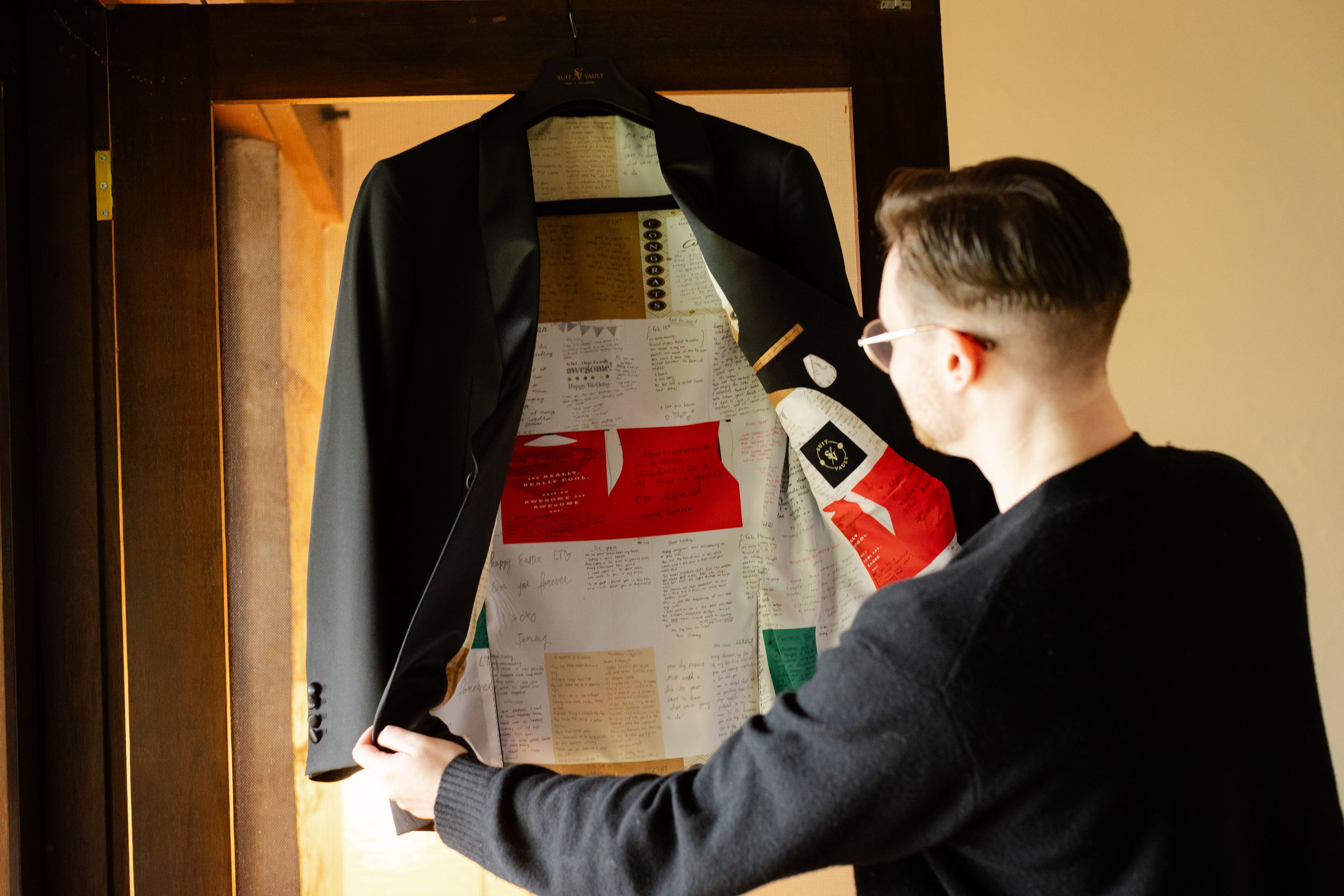 Candid photography of groom looking at his bespoke suit. The suit's lining is a  patchwork of best wishes from loved ones.