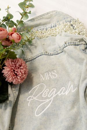Custom denim jacket decorated with pearls and 'MRS Rogah' paired with pink flowers. details from bride prep
