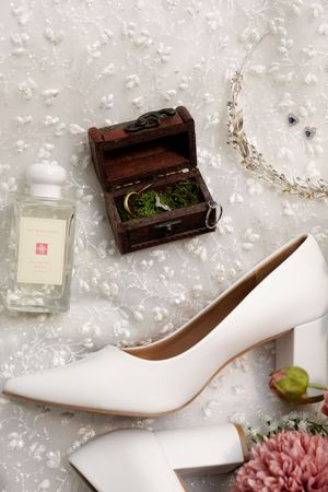 A pair of elegant white satin bridal pumps with pointed toes displayed against a light floral background.