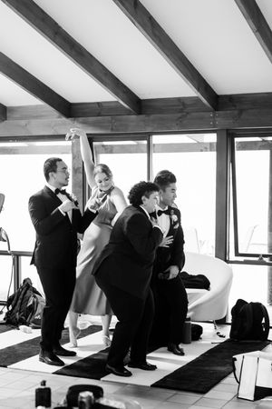 Black and white photo of wedding party members sitting casually together near large windows.