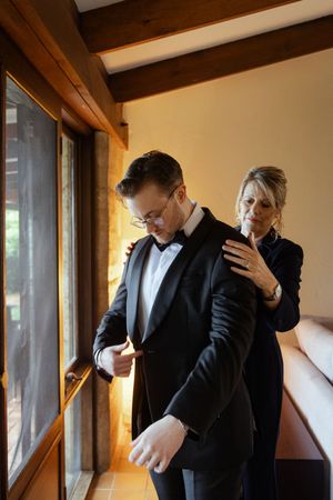 A sequence of formal getting ready moments showing dark suit adjustments in warm indoor lighting.
