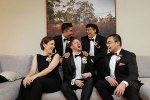 Wedding party laughing together on couch in formal black tie attire.
