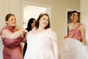 Wedding party members in pink dresses celebrating and posing together in a bright room.