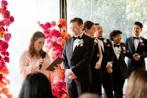 Wedding party dressed in black and white stands in line together with vibrant pink floral decor.