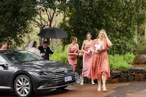 People gathered outside in formal attire next to luxury cars at an elegant outdoor venue during daytime event.