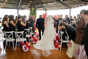 A panoramic view of an indoor wedding reception setup with white chairs and festive pink floral decorations.