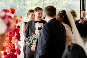 Wedding celebration in elegant venue with vibrant coral floral arrangements and large windows overlooking scenic view.
