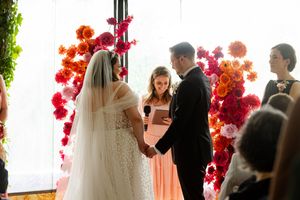 A wedding ceremony takes place in front of a stunning backdrop of vibrant red and pink floral arrangements.