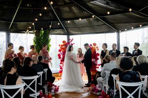 Wedding reception in bright indoor space decorated with pink balloon garlands and white chairs.