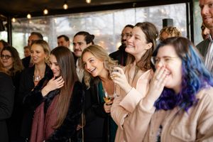 Crowd of guests laughing and enjoying themselves at an indoor event with warm lighting in the background.
