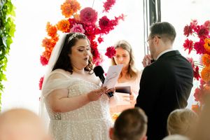 Romantic wedding dance scene with vibrant pink and orange paper flower wall decorations visible in background.