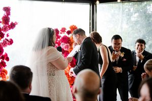 Wedding ceremony with vibrant red floral arrangements decorating the ceremony space by large windows.