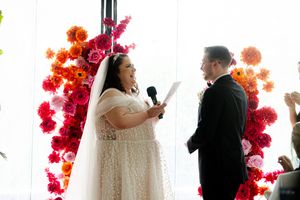 A wedding ceremony moment with vibrant orange and pink floral arrangements decorating the backdrop.