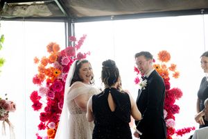 People gather in a bright indoor space with vibrant pink floral arrangements during what appears to be a social event.