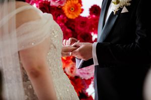 Close-up of wedding rings being exchanged against a backdrop of bright pink and red flowers.