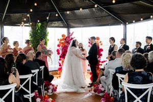 Wide view of wedding ceremony with white dresses and red floral arrangements against bright windows.