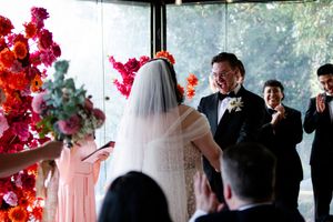 A romantic wedding ceremony with bright red floral arrangements and guests watching as the couple exchanges vows.