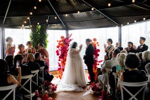 Indoor wedding ceremony with white chairs and a stunning red and pink floral arch installation.
