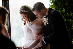 A joyful wedding couple shares an intimate moment under a floral arch with pink and red blooms.