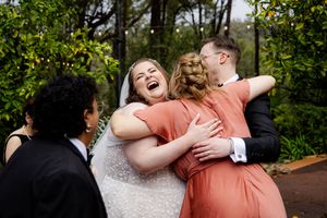 bridesmaid hugging bride and groom after their wedding ceremony