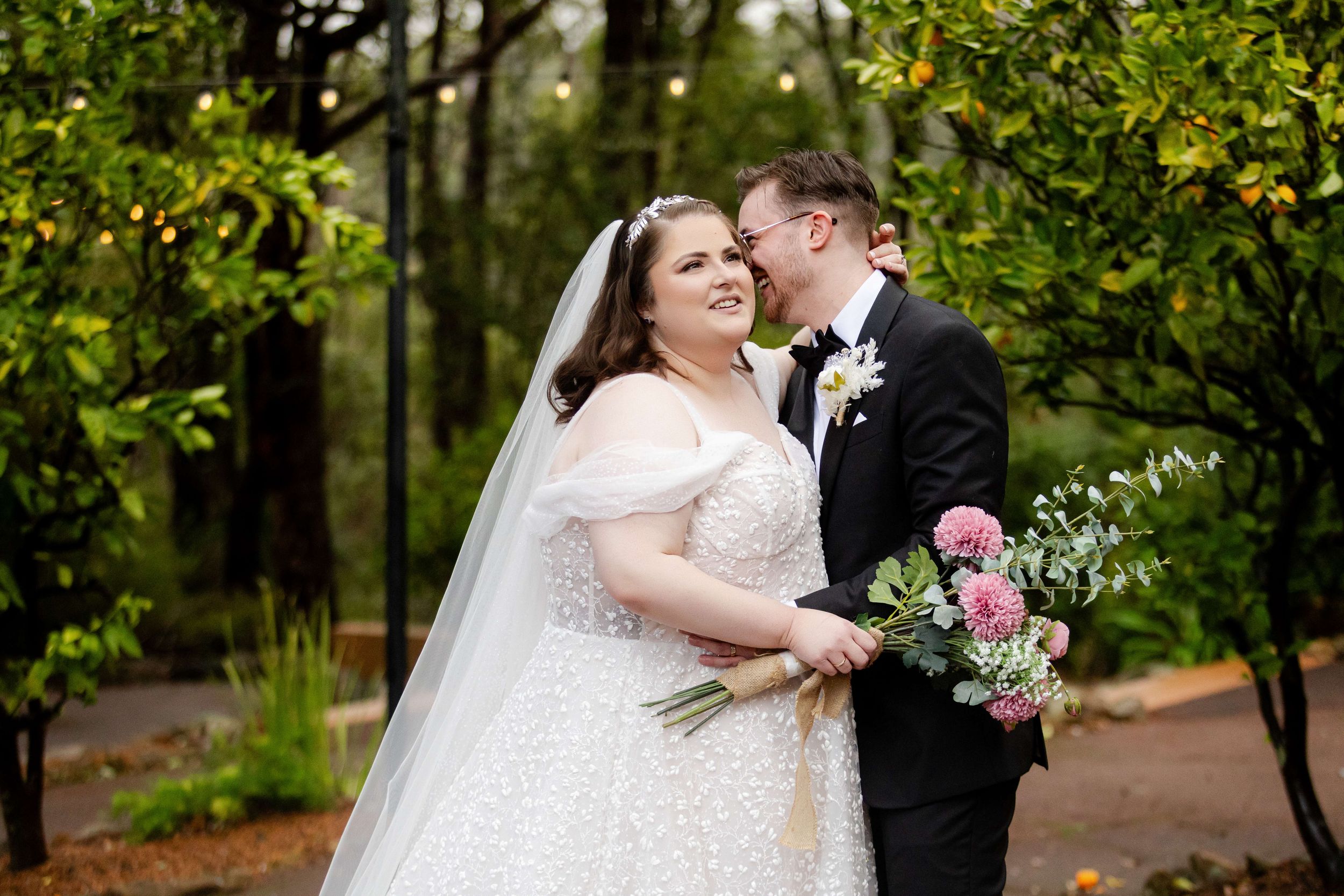Romantic outdoor wedding portrait of a couple surrounded by lush greenery in a garden setting.