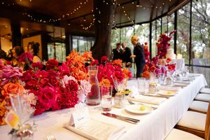 Elegant wedding reception table decorated with vibrant red floral centrepieces and place settings in a bright venue.