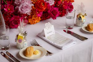 Elegant wedding table setting with bright pink and red roses, menu cards, and place settings on white linens.