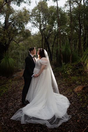 Romantic wedding couple shares intimate moment in a lush wooded forest setting with flowing white dress and veil.