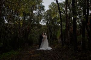 A person in a white wedding dress poses in a forested area with fall foliage and natural lighting.