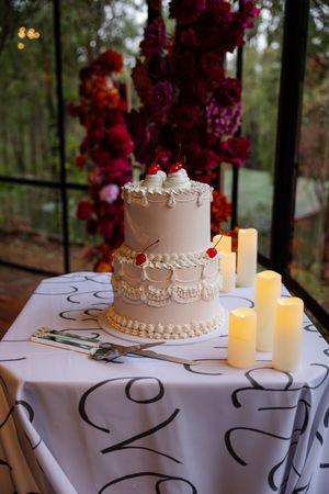 vintage Three-tiered pink wedding cake decorated with lace patterns and topped with cherries alongside glowing candles.