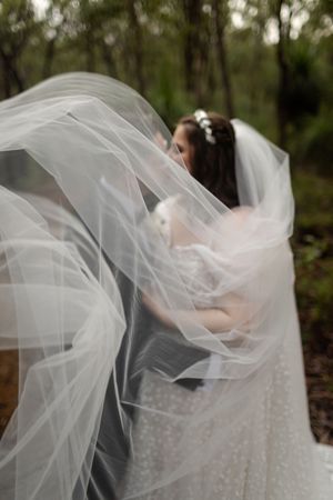 Flowing white wedding veil and dress captured in dreamy motion against a natural forest backdrop.