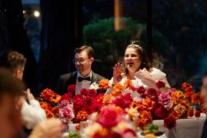 Wedding reception dinner table decorated with vibrant red and orange floral arrangements and soft lighting.
