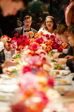 A wedding reception table decorated with vibrant pink and orange floral centerpieces.