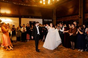 Wide shot of a wedding reception venue with guests watching the bride and groom perform their first dance. Wedding photography