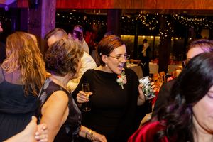 Wedding guests enjoying drinks and dancing at lively reception with colorful lighting.