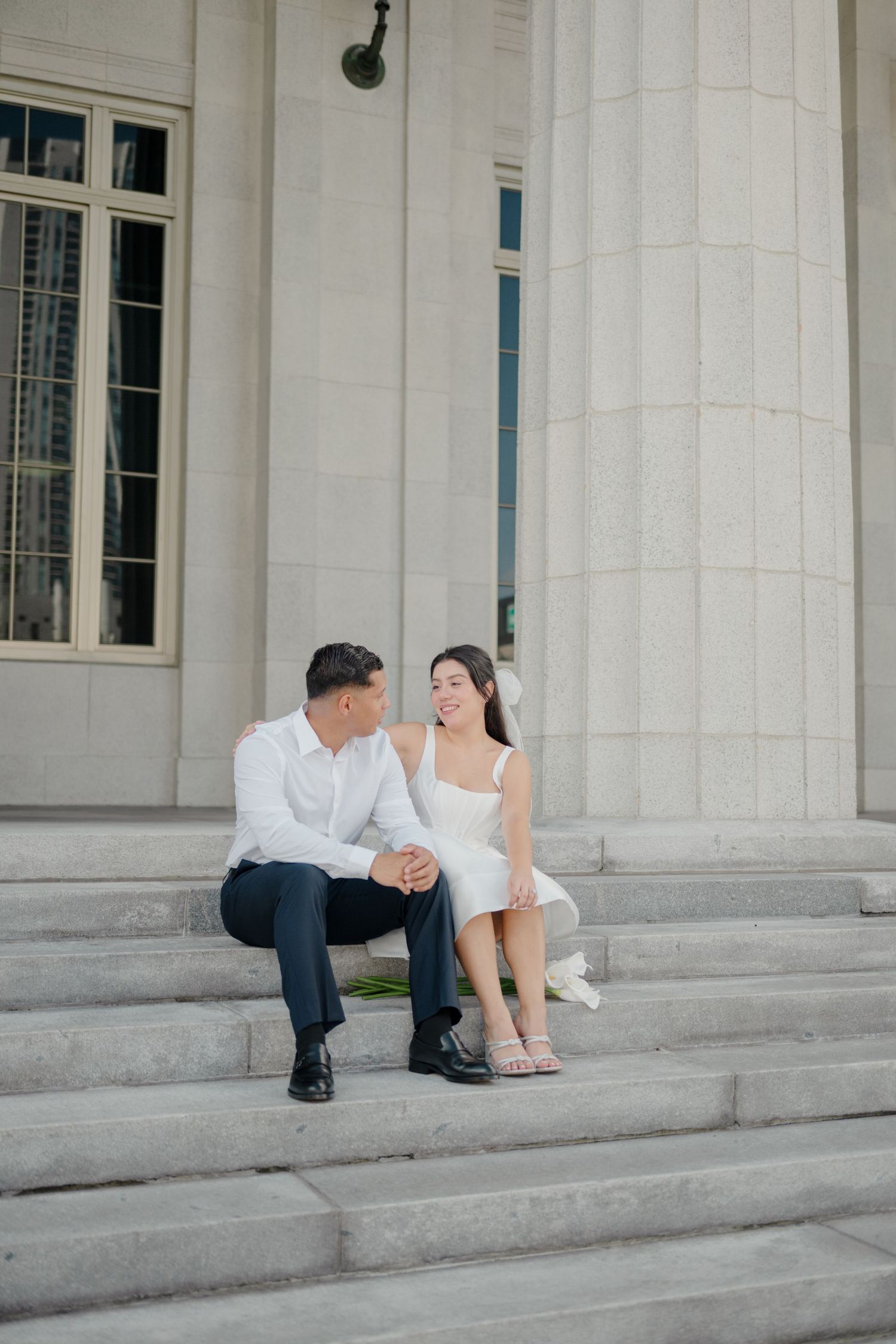 A couple shares a romantic moment on the grand steps of a classical building with white columns.