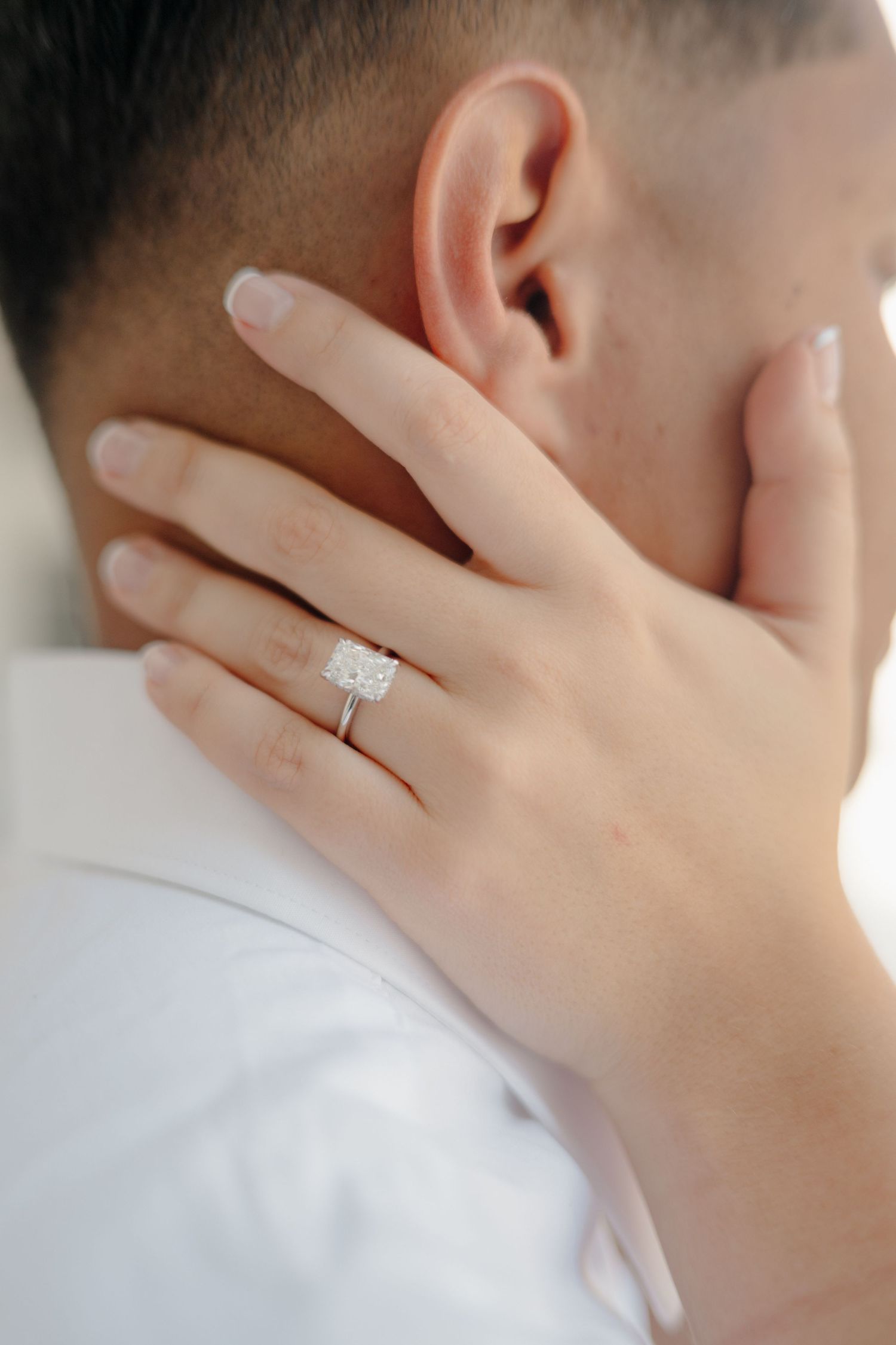 Close-up of hands wearing a sparkling diamond engagement ring against a white background.