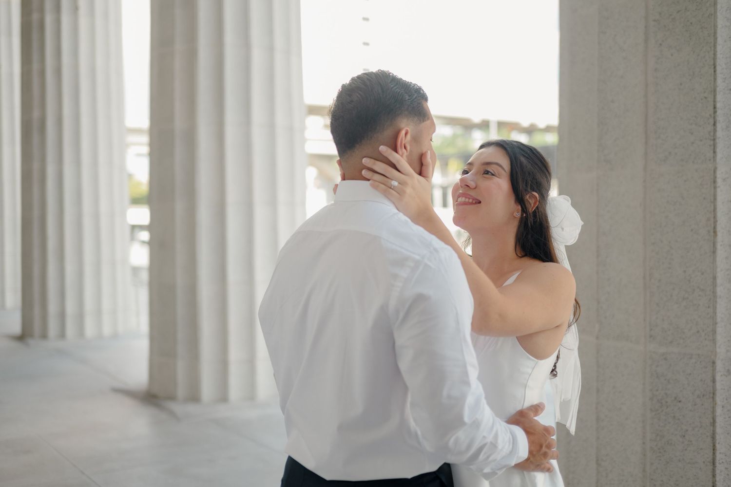 Romantic couple in formal attire embraces intimately against a backdrop of white columns in an elegant setting.