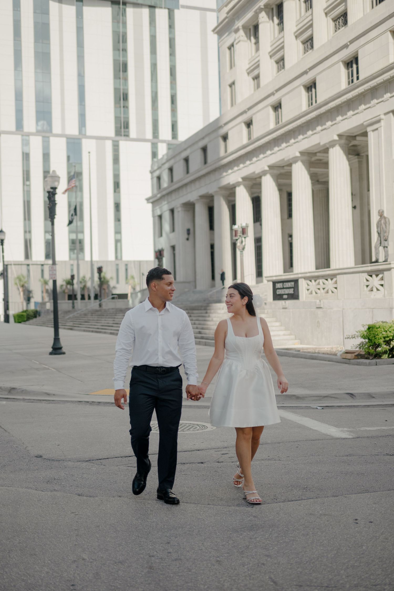 A couple walks hand in hand through a grand colonnade of a historic white stone building.