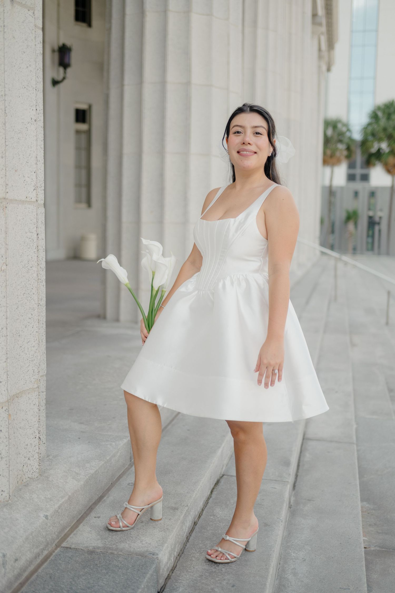 A series of close-up shots showing white heels and a flowing white dress against a light stone column background.
