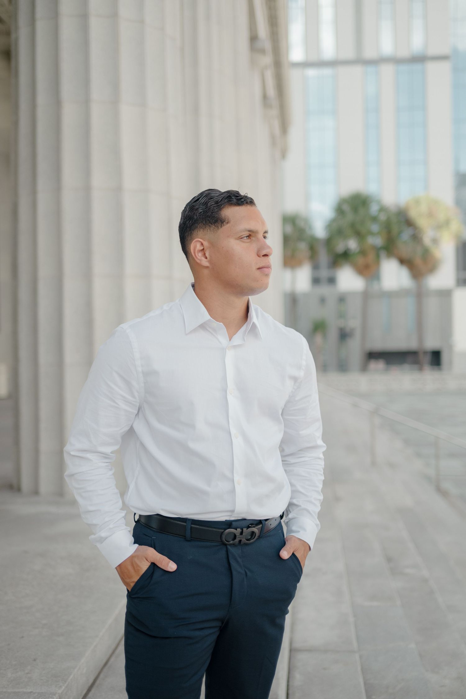 Professional portrait session showing a person in a crisp white dress shirt and navy pants against a light architectural backdrop.