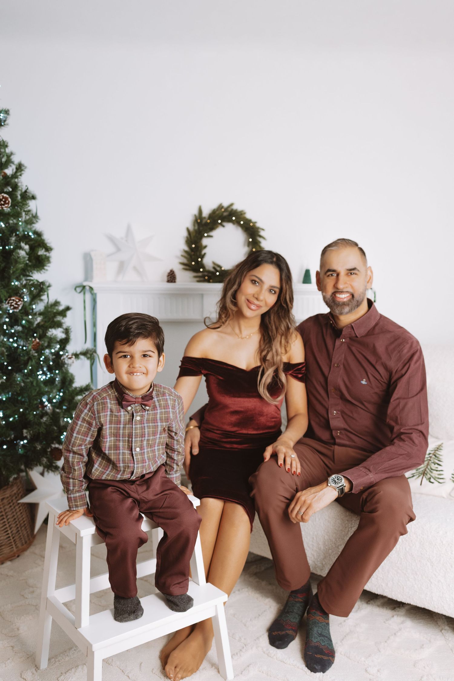A family poses together in coordinated brown outfits for a cozy holiday photoshoot near a decorated Christmas tree.