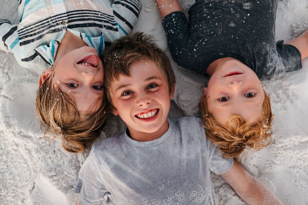 Three children lying on the ground together, looking up at the camera with joyful expressions.