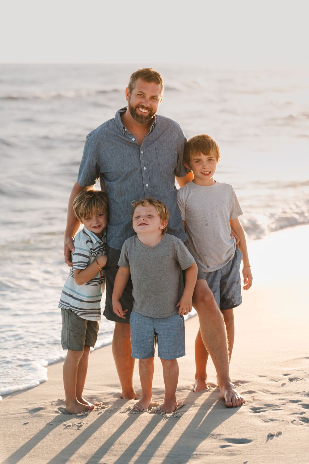 A family enjoying a sunset moment together on a sandy beach with long shadows cast behind them.