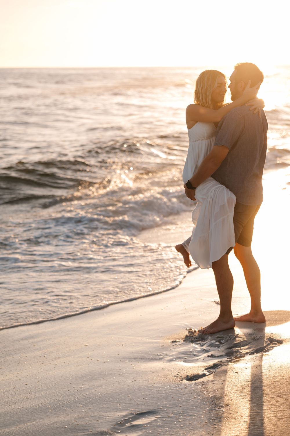 Couple standing together at the beach shoreline during golden sunset hour.